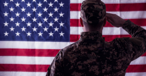 Healthcare Operations & Practice Management Blog | Integral Clinic Solutions 9 A cinematic, rear-view shot of a military service member in camouflage uniform saluting a large American flag, featuring a professional and atmospheric deep purple color overlay to match brand aesthetics.
